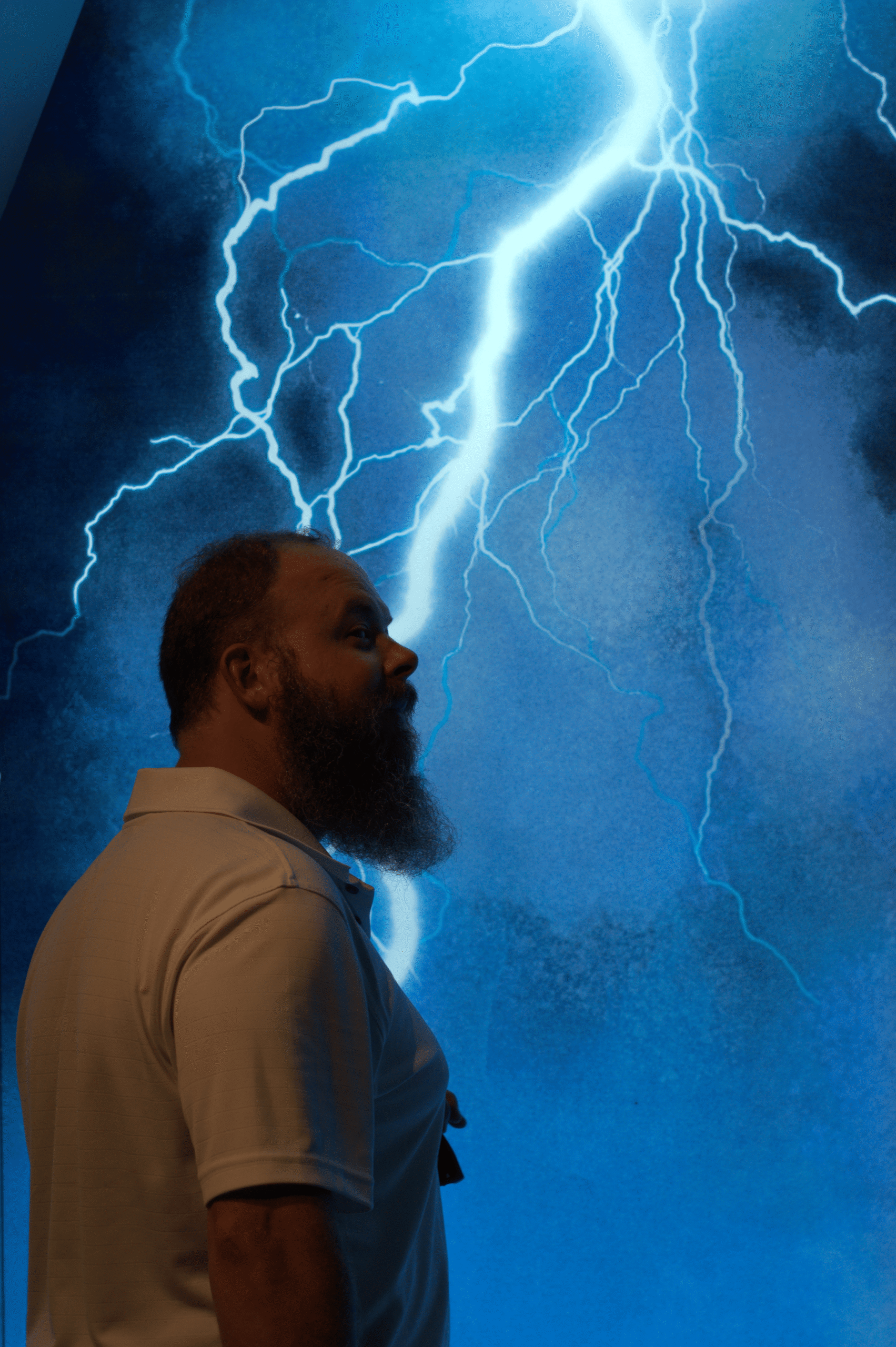 An artistic photography shot of a man standing against a background of blue lightning. 